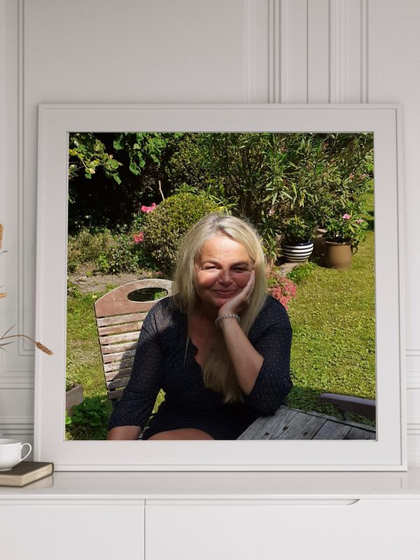 Claudia Stanitzeck in einem weißem Rahmen auf einem kleinem Regal.