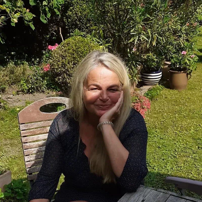 Lebe liebe Berufung, Claudia Stanitzeck sitzt an einem Tisch in ihrem Garten und genießt lächelnd die Sonne.